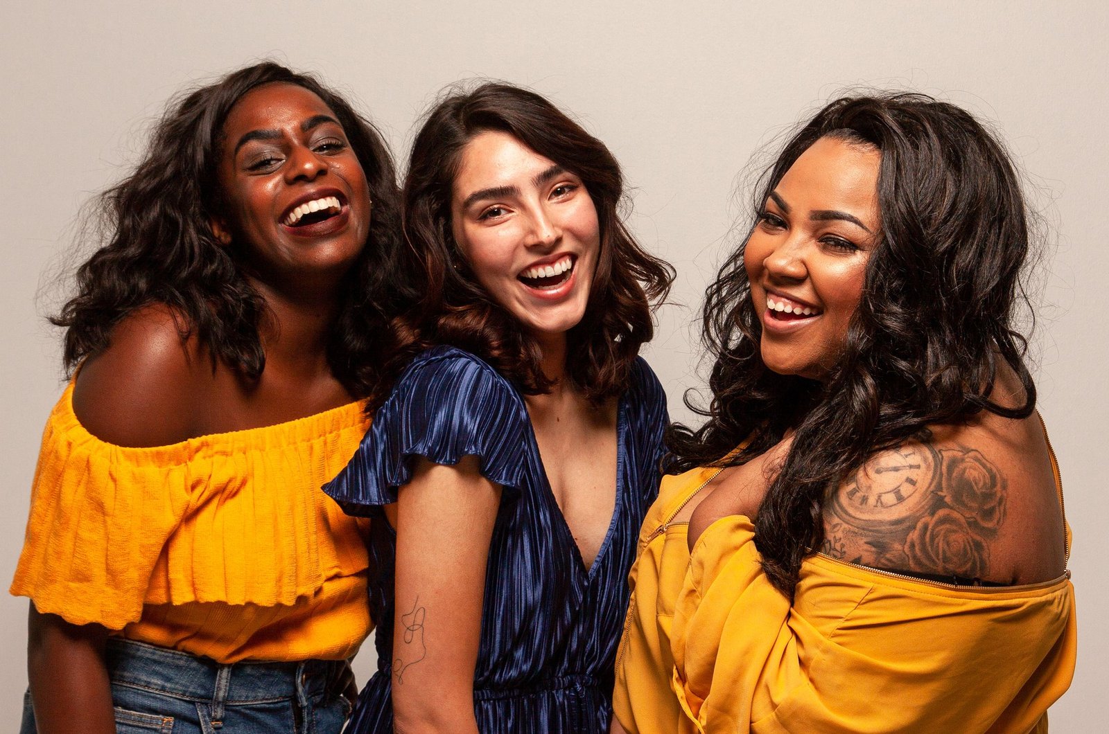 Three women wearing colourful dresses and smiling together